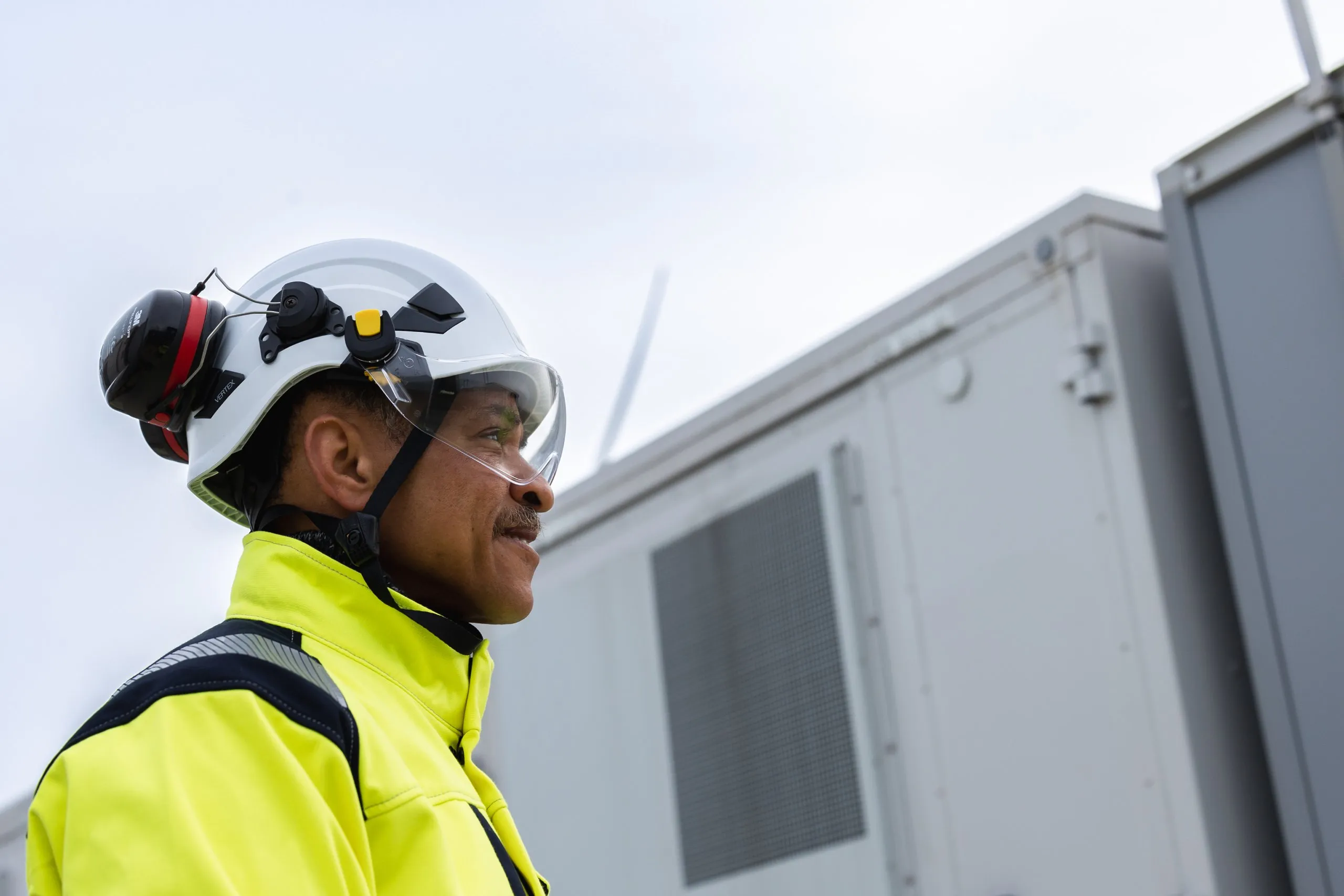 Technician in hard helmet and high visibility in front of storage unit.